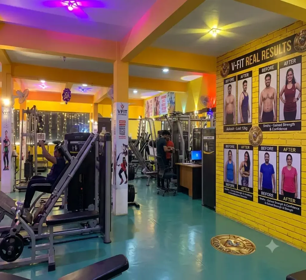 V-Fit Gym and Fitness Studio interior in Vadavalli featuring modern training equipment and member transformation wall